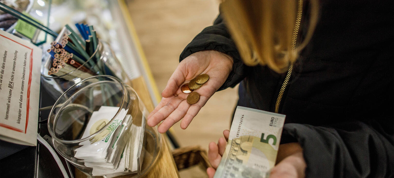 Junge Frau steht an der Kasse einen Supermarktes mit Geld in der Hand - PM Inflationsmonitor