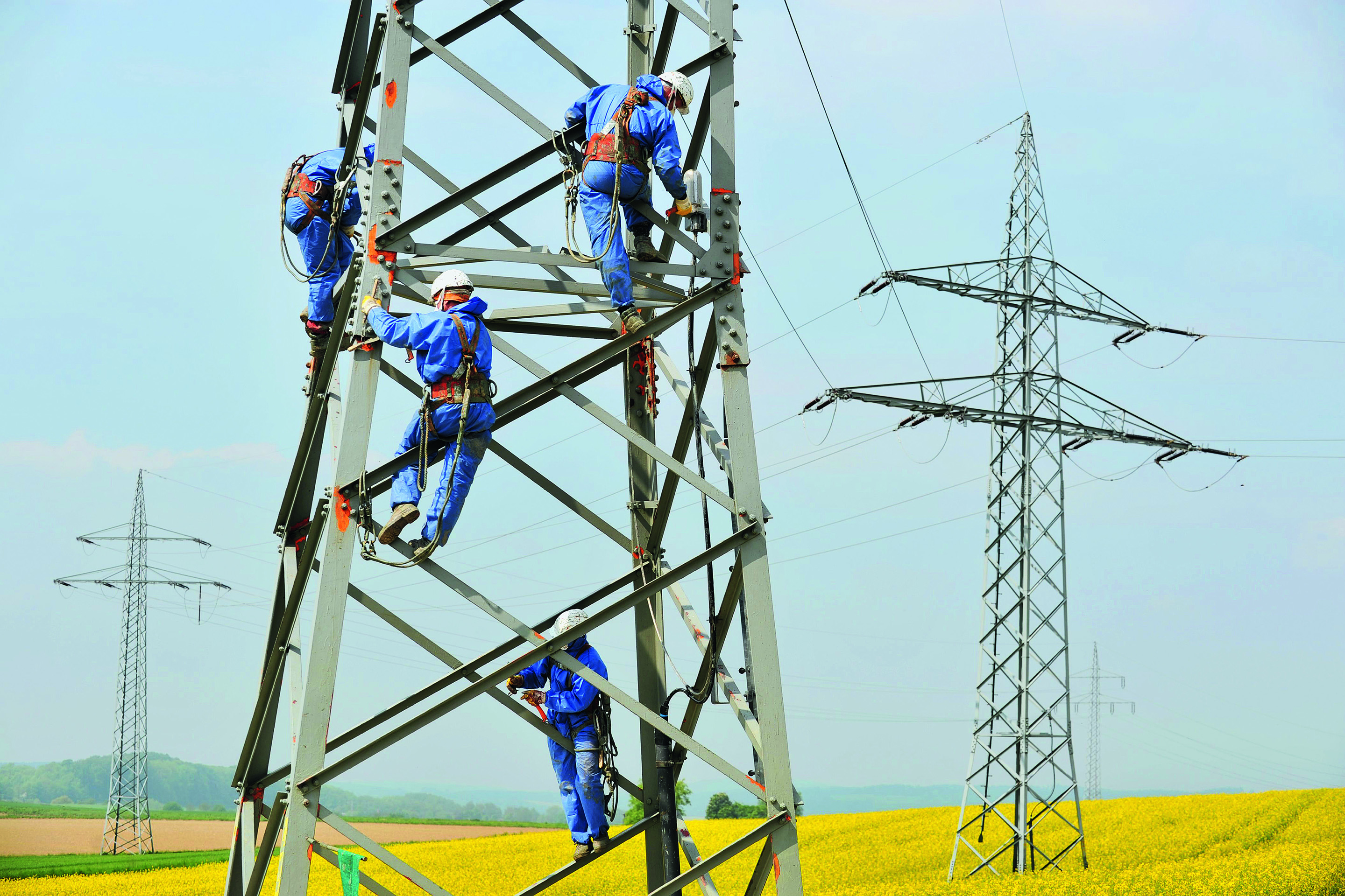 Polnische Arbeiter sind dabei, den Rostschutz an einem Strommast zu erneuern.