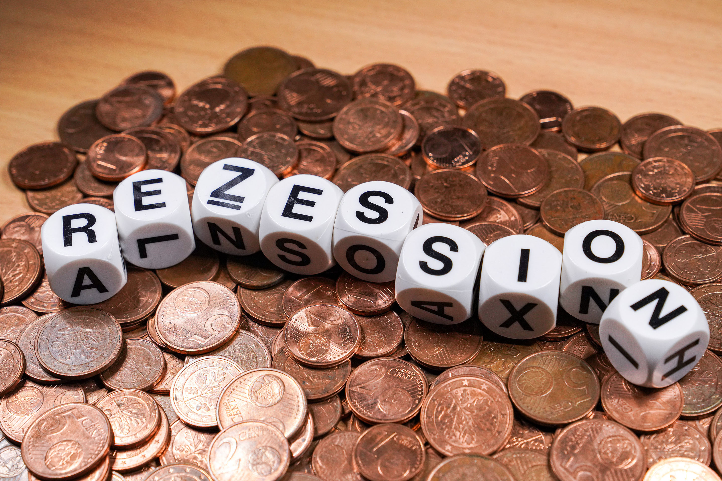 Konjunkturindikator - Diverse Würfel liegen auf einem Teppich aus Centstücken und bilden das Wort Rezession