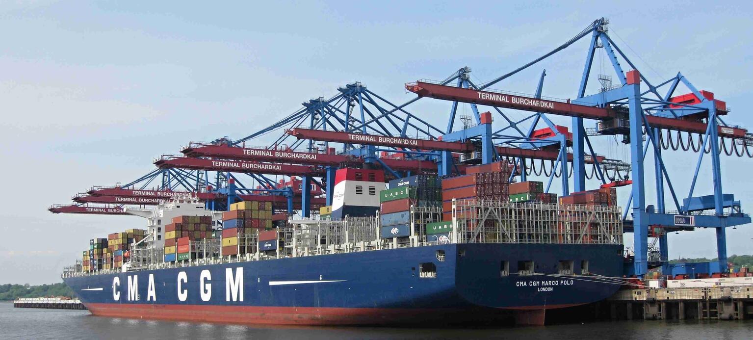 Containerschiff im Hafen mit Kränen zur Be- und Entladung im Hintergrund