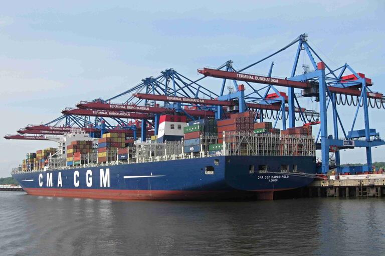 Containerschiff im Hafen, im Hintergrund Kräne zur Be- und Entladung