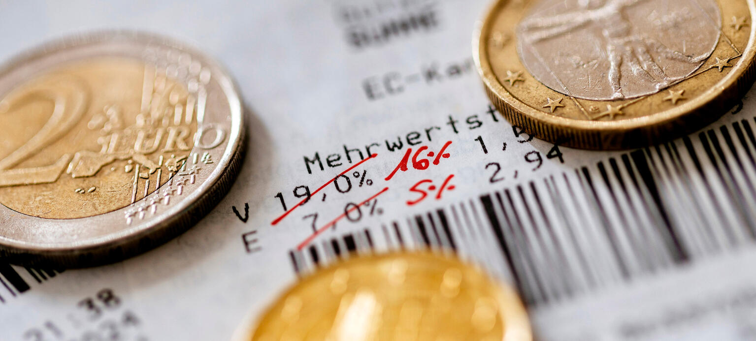 Euro Münzen liegen auf einem Kassenbon auf dem die gesenkte Mehrwertsteuer steht