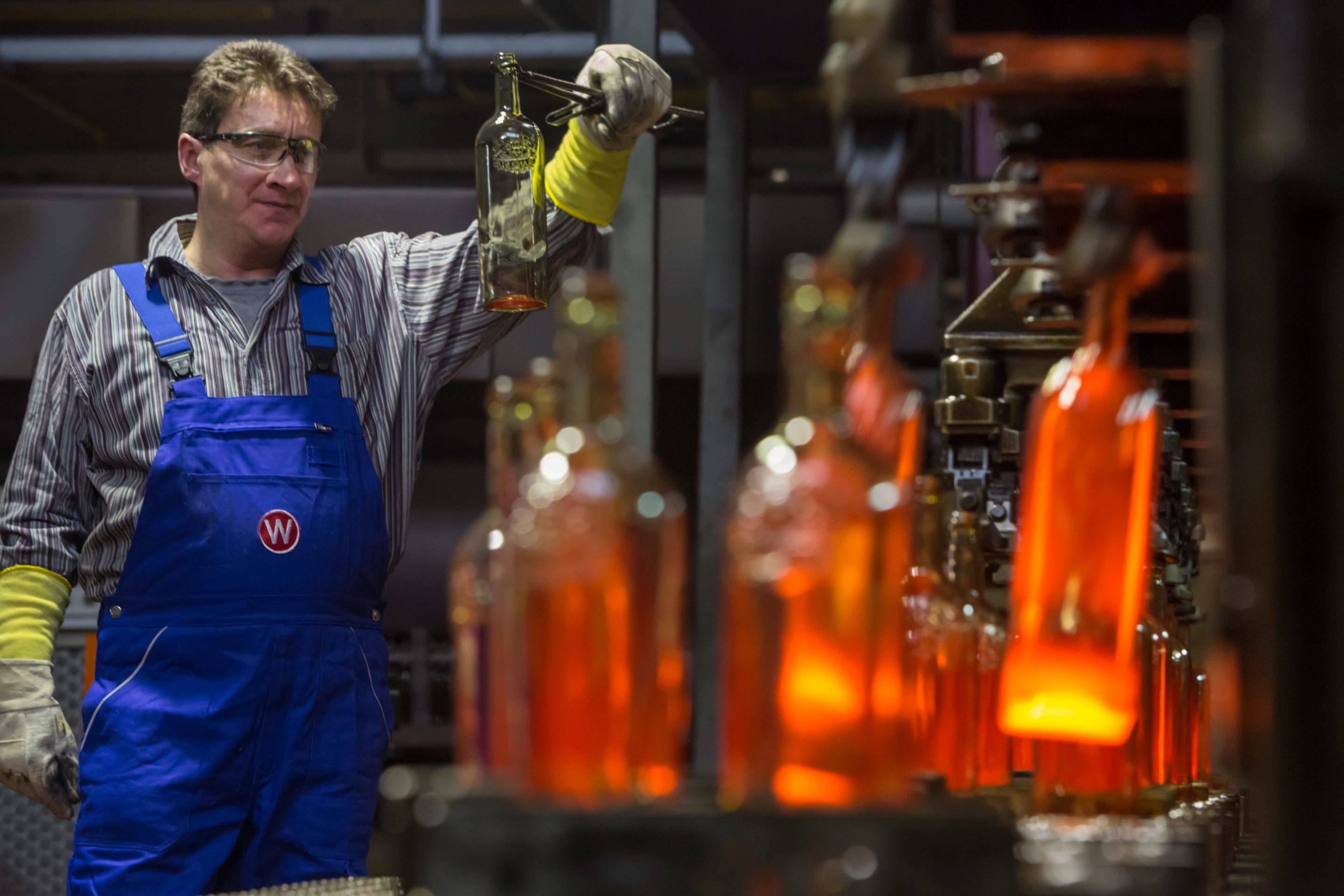 Ein Arbeiter prüft eine noch warme Glasflasche in der Herstellung